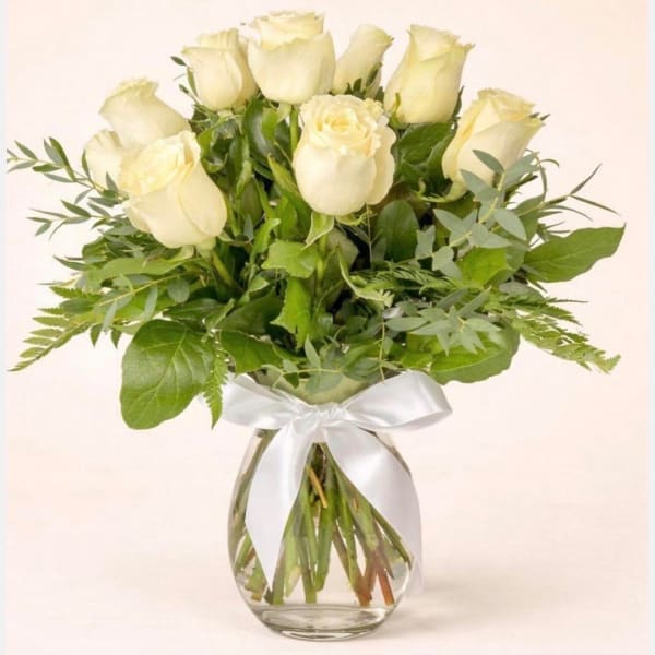 White roses arranged in a clear glass vase with a white ribbon