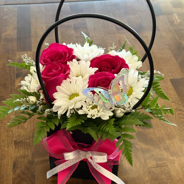 Pink roses and white daisies in a black handled basket with a butterfly pick