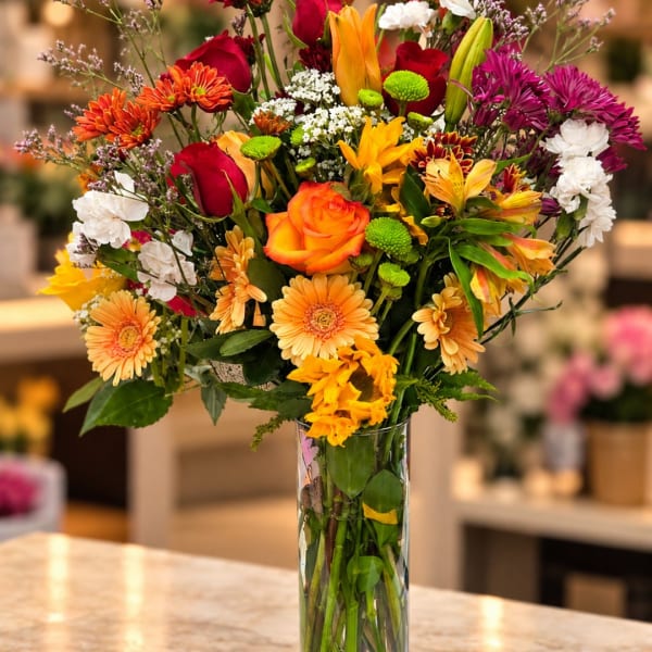 Mixed bouquet of roses, gerbera daisies, and lilies in a clear glass vase