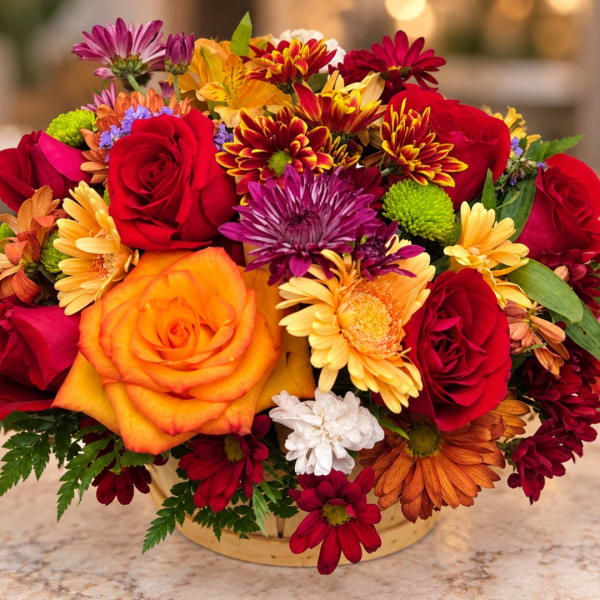 Mixed bouquet of red and orange roses with colorful daisies in a low basket