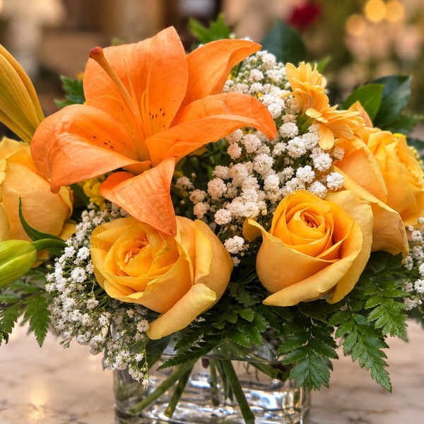 Orange lilies and yellow roses in a clear glass vase