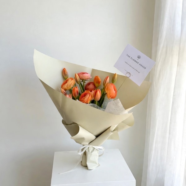 Bouquet of orange and pink ranunculus wrapped in cream paper