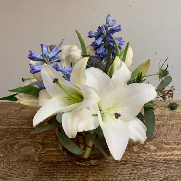 White lilies and blue flowers arranged in a glass vase