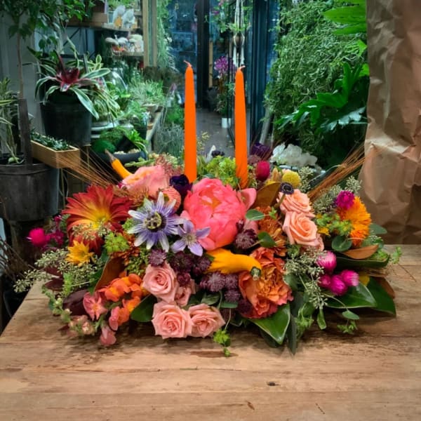 Colorful floral arrangement with tall orange candles on a wooden table