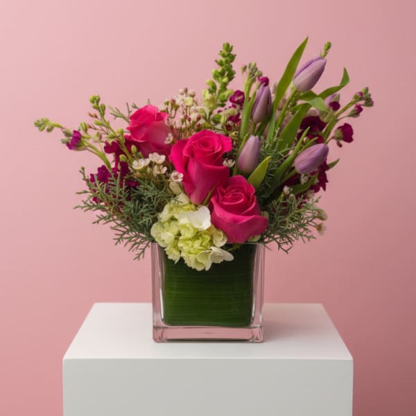Pink roses and purple tulips in a square glass vase