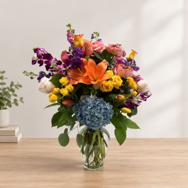 Colorful mixed bouquet in a clear glass vase with lilies, roses, and hydrangea