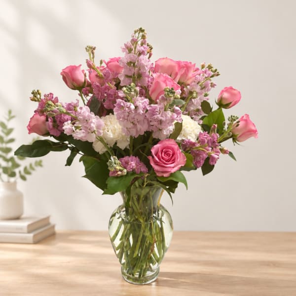 Pink roses and lilac flowers arranged in a clear glass vase