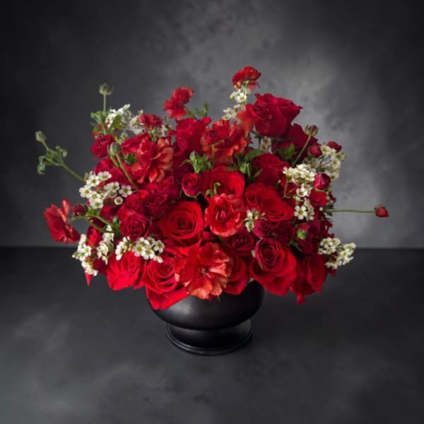 Red rose arrangement in a black vase with small white filler flowers