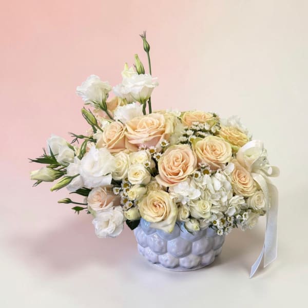 Cream roses and white flowers in a textured ceramic vase with a ribbon