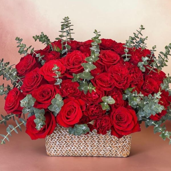 Red roses arranged in a woven rectangular basket with eucalyptus sprigs