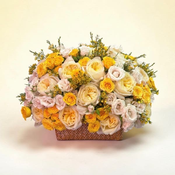 Bouquet of yellow, cream, and pale pink roses in a rectangular vase