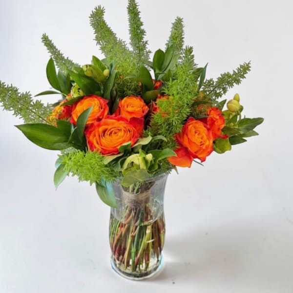 Orange roses in a clear glass vase with green foliage