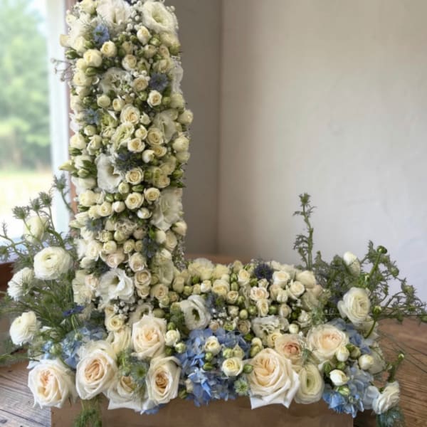 White floral cross arrangement with blue accents on a table