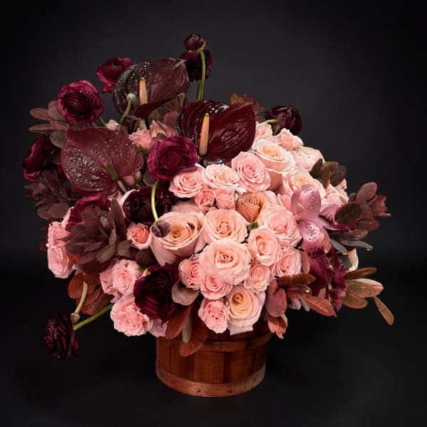 Pink and burgundy roses with dark anthuriums in a wooden basket