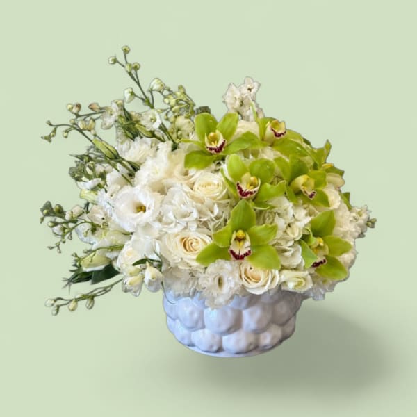 White floral arrangement with green orchids in a textured white vase