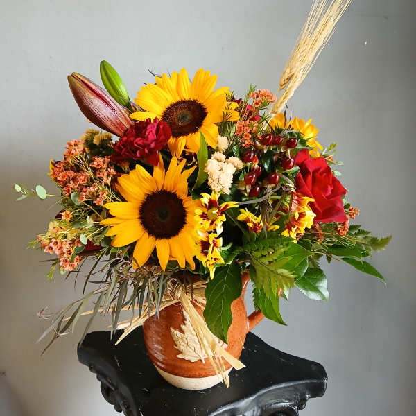Sunflower arrangement in a ceramic vase with red roses and wheat accents