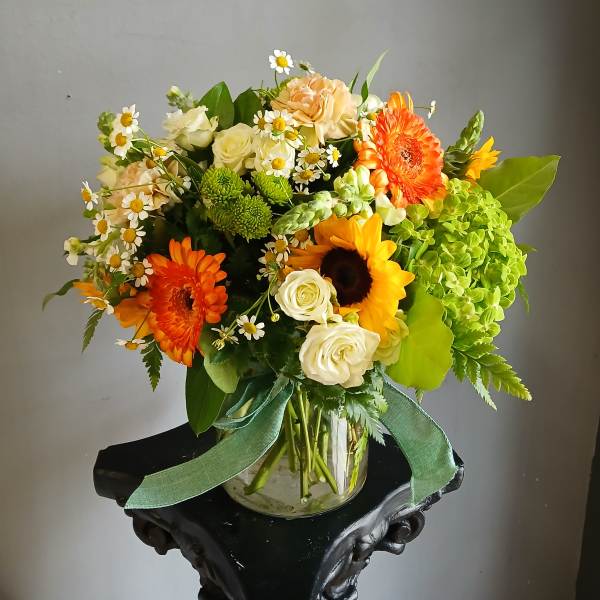 Mixed bouquet in a glass vase with orange gerberas, sunflowers, white roses, and green hydrangea