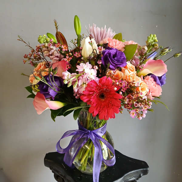 Colorful mixed bouquet in a glass vase tied with a purple ribbon