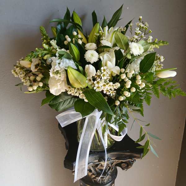 White floral bouquet in a glass vase with a white ribbon