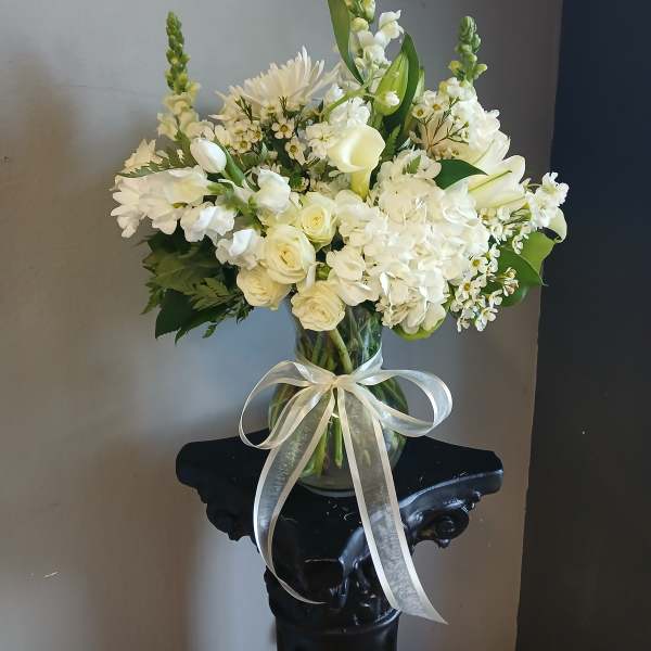 White floral arrangement in a glass vase with a sheer ribbon bow