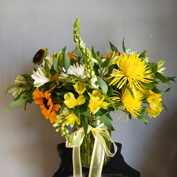 Mixed yellow, white, and orange flowers arranged in a glass vase with a ribbon