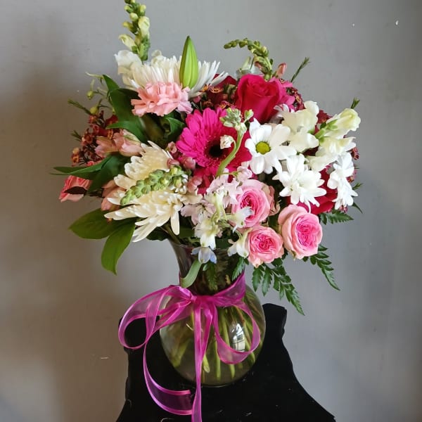 Mixed bouquet of pink, white, and red flowers in a glass vase with a pink ribbon