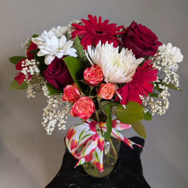 Mixed bouquet of red, white, and pink flowers in a glass vase with a floral ribbon