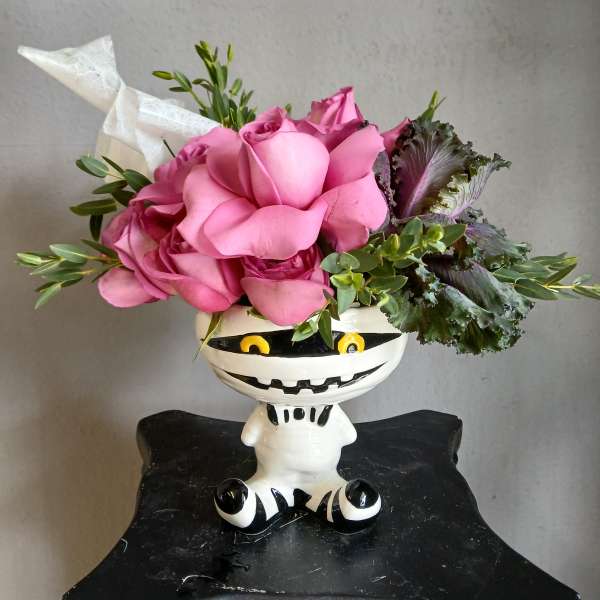 Pink roses arranged in a white Halloween-style vase with green foliage