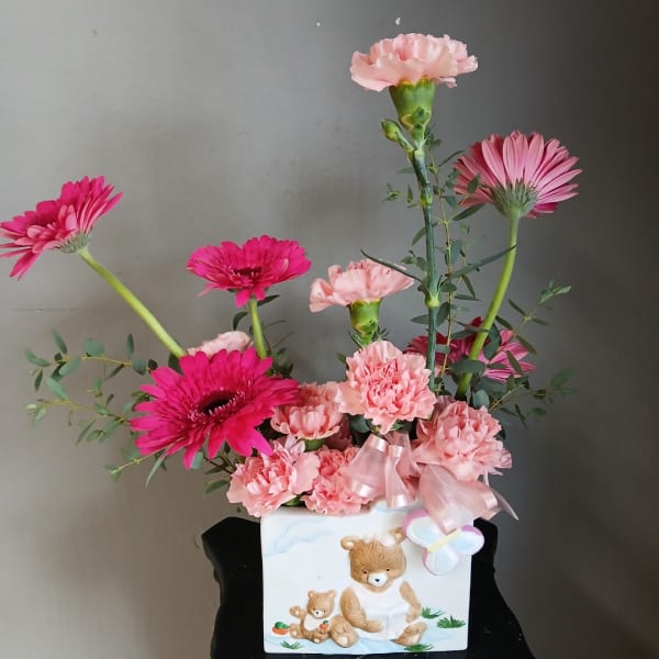 Pink carnations and gerbera daisies in a white teddy bear vase