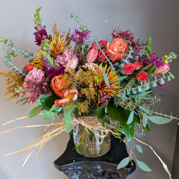 Mixed bouquet of roses, tulips, and purple blooms in a glass vase