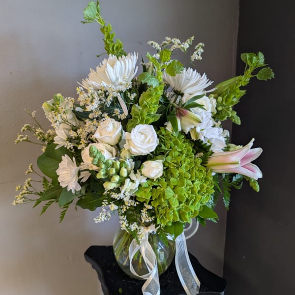 White roses and lilies with green hydrangea in a glass vase