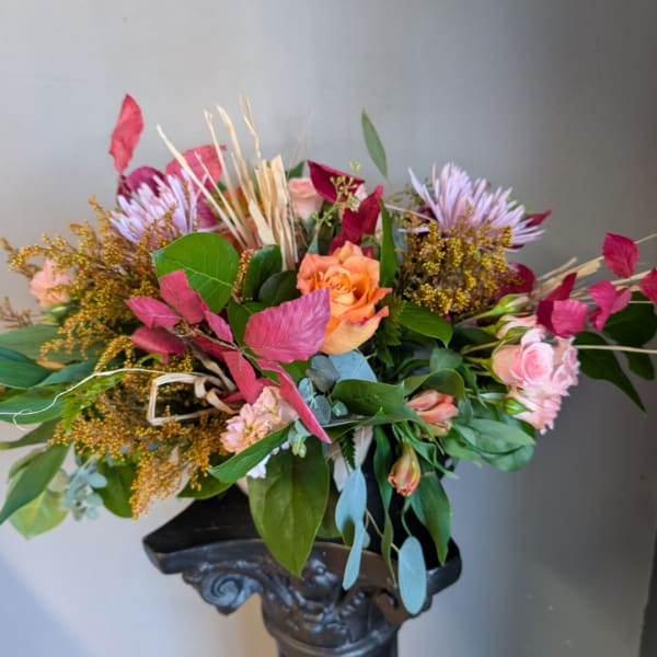Mixed bouquet with peach roses, pink blooms, and purple flowers in a dark vase
