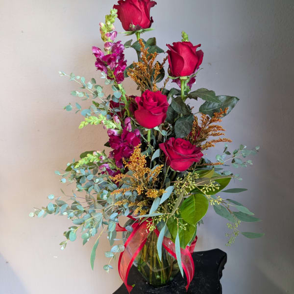 Tall bouquet of red roses and purple flowers in a glass vase with a red ribbon