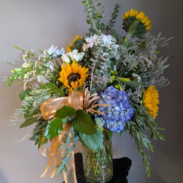 Bouquet of sunflowers, white blooms, and blue hydrangea in a glass vase