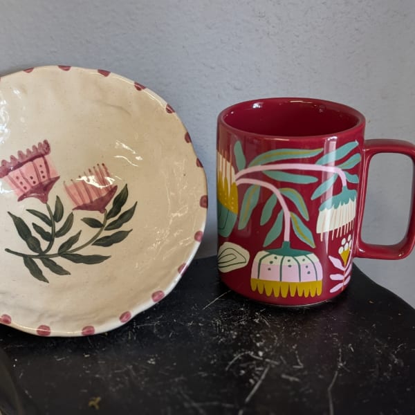 Decorative floral plate beside a red mug with painted flowers