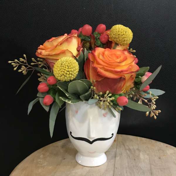Orange roses in a white face vase with yellow pom flowers