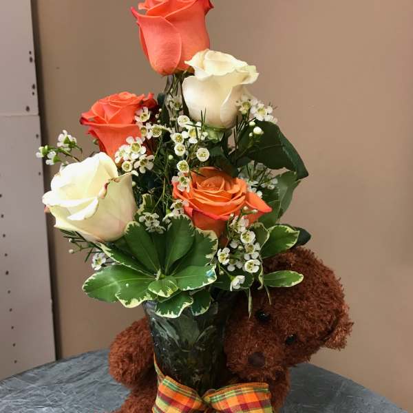 Bouquet of orange and white roses in a vase with a teddy bear