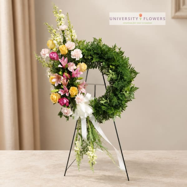 Floral wreath on a stand with pink, yellow, and white blooms