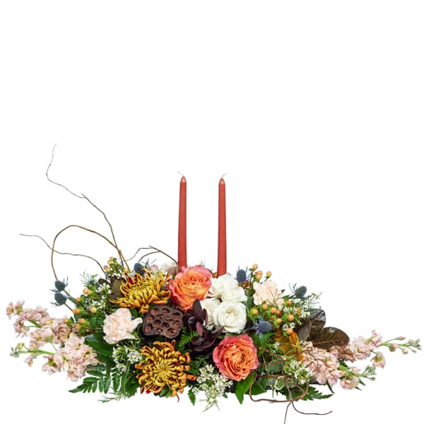 Low floral centerpiece with two red taper candles and orange, white, and pink blooms
