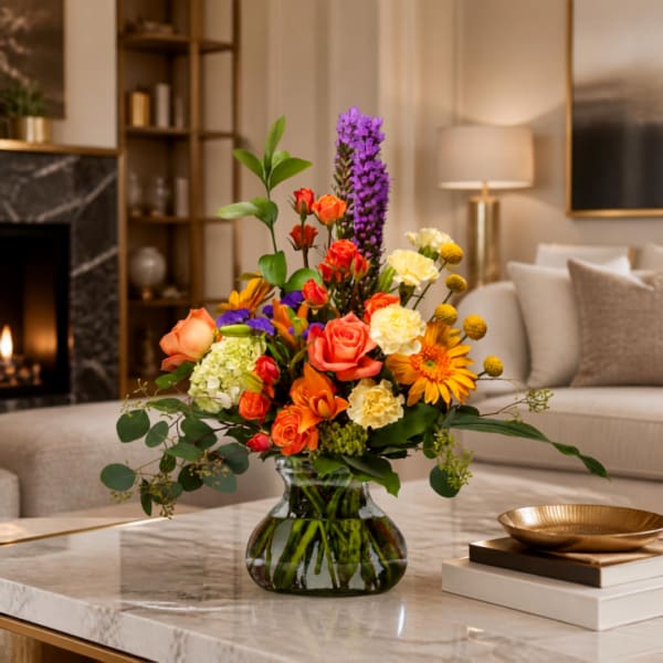 Mixed bouquet of orange, pink, yellow, and purple flowers in a glass vase