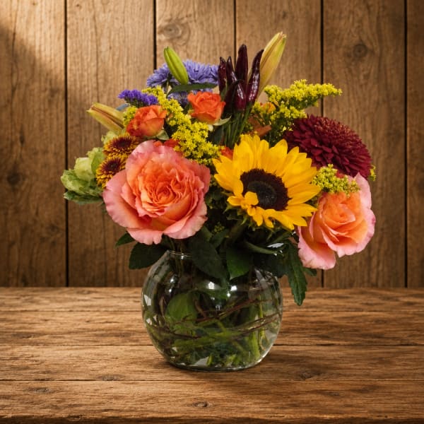 Mixed bouquet of roses, sunflowers, lilies, and chrysanthemums in a glass vase