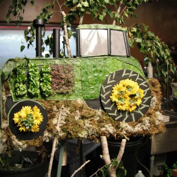 Green tractor-shaped floral display with yellow flower wheels