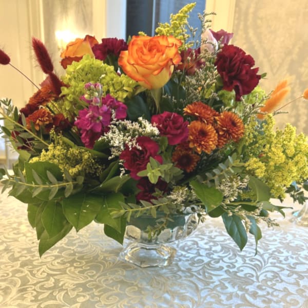 Mixed bouquet of orange and burgundy flowers in a clear glass vase