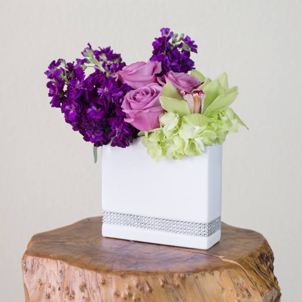 Purple and pink roses with green orchids in a white vase