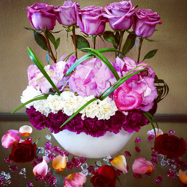 Pink roses and carnations arranged in a white bowl with decorative petals.