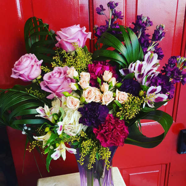 Mixed bouquet of pink, purple, and white flowers in a purple glass vase