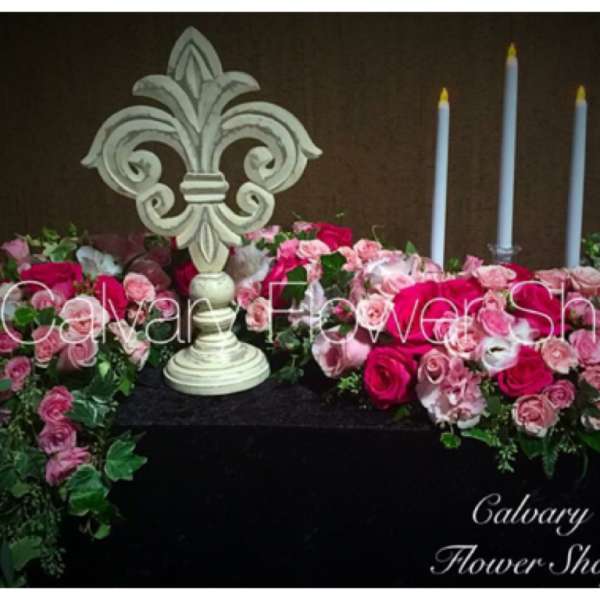 Pink rose arrangements with a decorative fleur-de-lis and tall candles