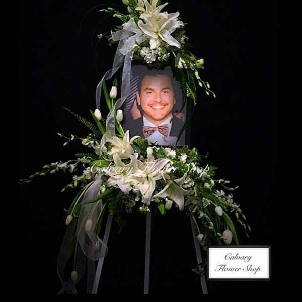 White lily funeral spray around a framed portrait on a stand