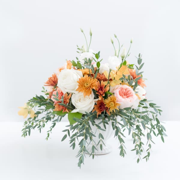 Mixed bouquet of white, peach, and orange flowers in a white vase