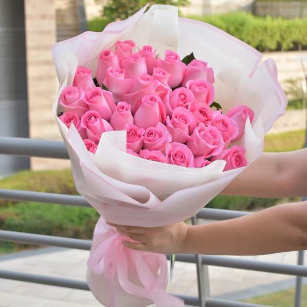 Hand-tied bouquet of many pink roses wrapped in white paper with a pink ribbon